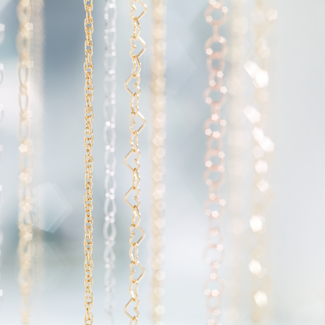 A close-up picture of hanging delicate gold chain with various sizes and forms of chain links for Forever Linked permanent jewelry with a light blue background | Peterson MADE