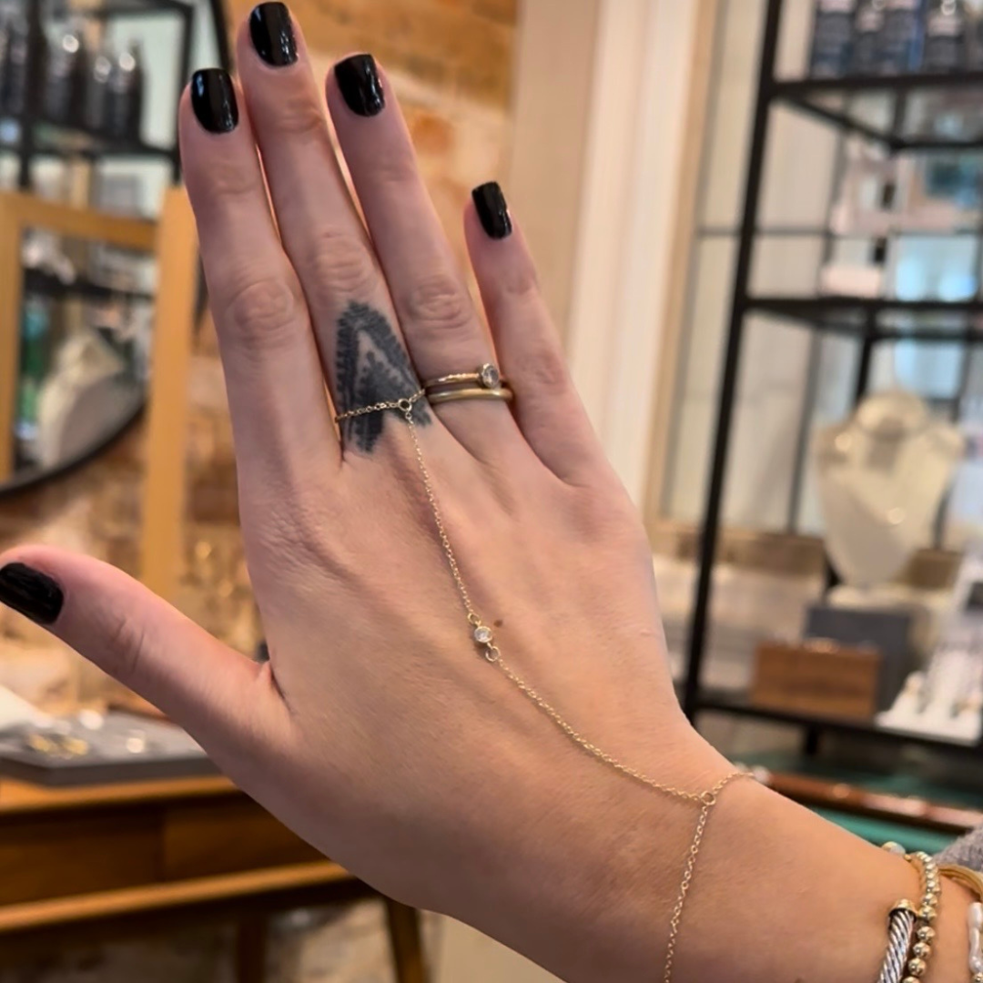 A close up image of a woman's hand featuring a new custom-fit 14k gold hand chain with a diamond bezel link with the background of Peterson MADE's studio