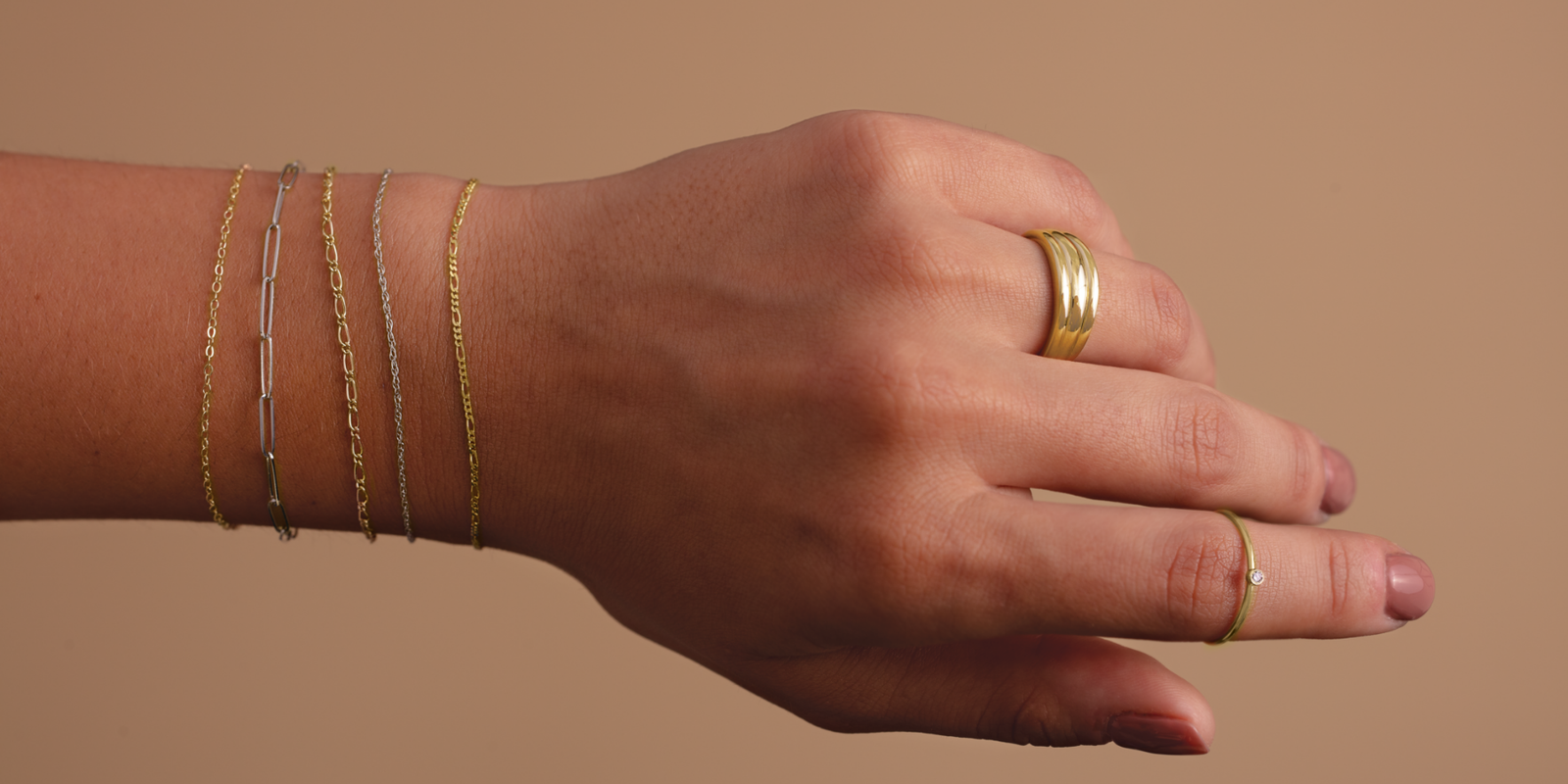 A woman's hand and wrist on a neutral background wearing 14k gold Forever Linked permanent Jewelry | Peterson MADE
