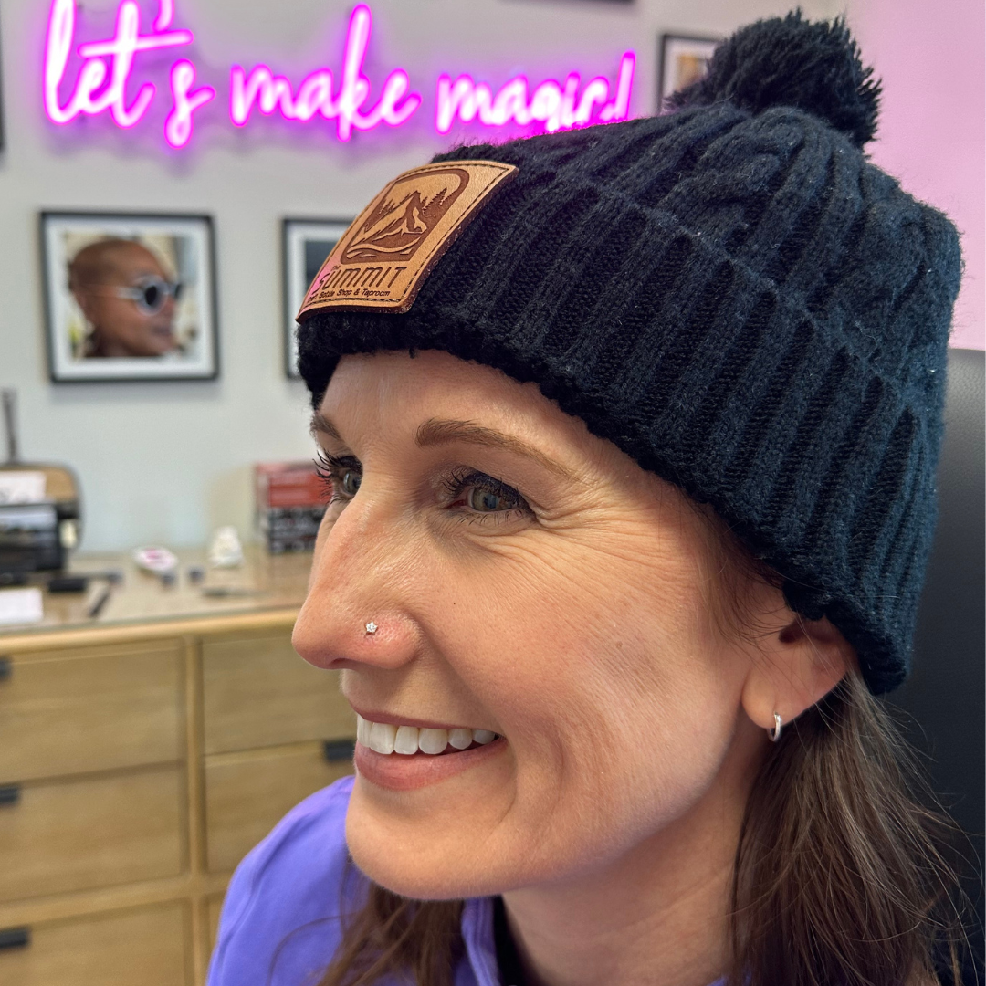 A smiling woman with a new nostril piercing wearing a hat. 