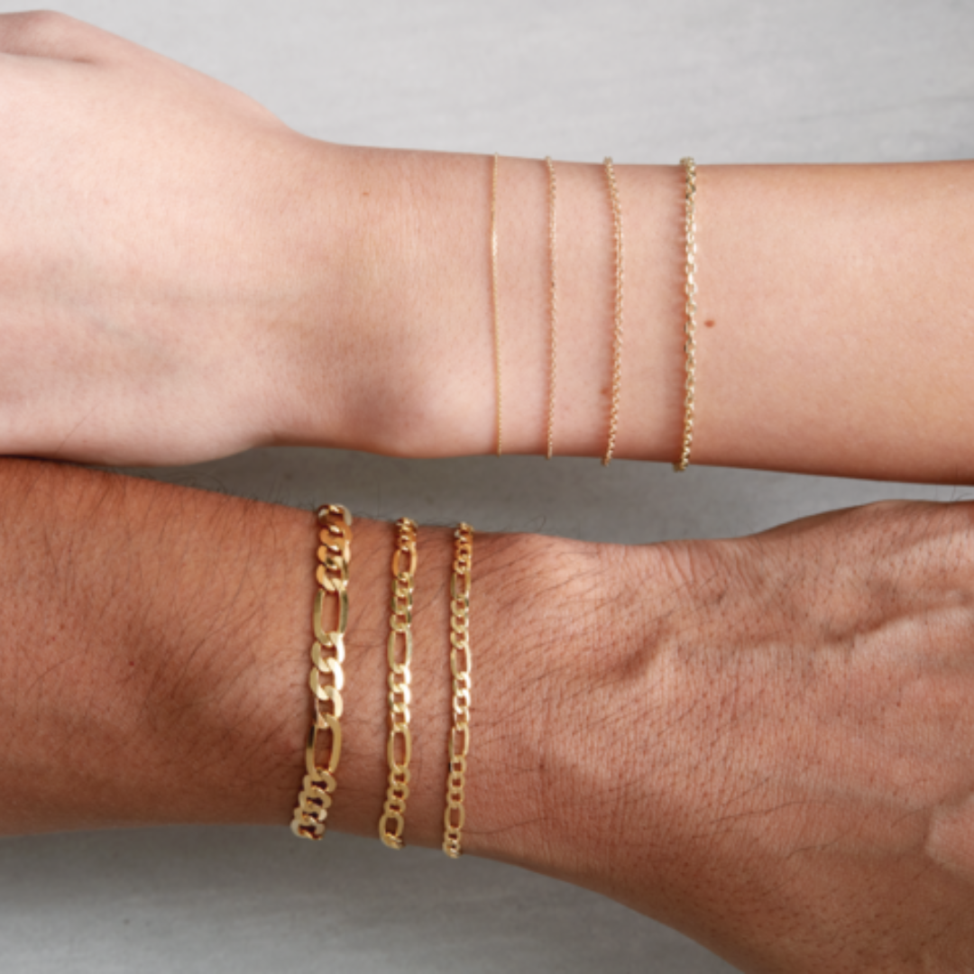 A picture of a woman's and a man's wrist - both wearing 14k gold chains of different varieties and weight - in front of a neutral background. Special Orders available at Peterson MADE